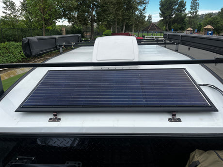 Overhead view of an RV rental roof featuring a large solar panel, roof rack, and side awnings for off-grid adventures.