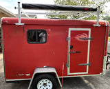 Red cargo trailer, modified with window, solar-ready roof rack, & awning for RV rental.