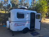 Compact white Scamp travel trailer RV rental, door open & ready for adventure.
