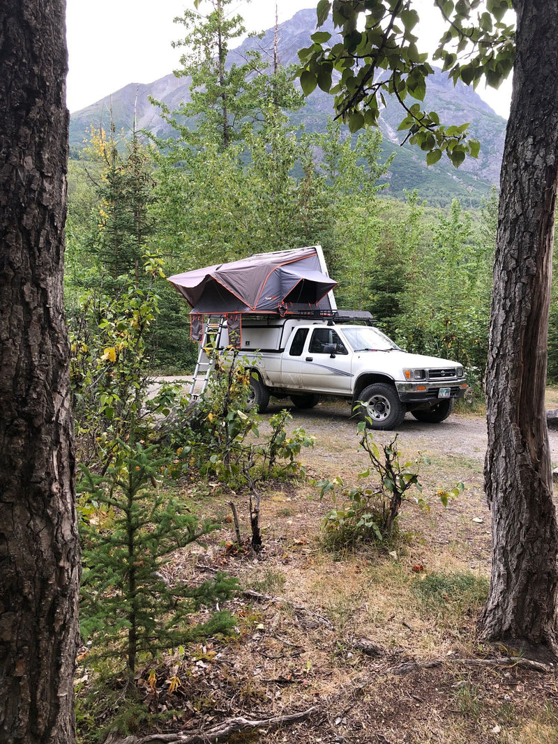  ideal for mountain adventures.|White truck with a rooftop tent set up in a forested mountain campsite. A versatile option for an RV rental adventure.|White pickup truck with a deployed rooftop tent — photo 2