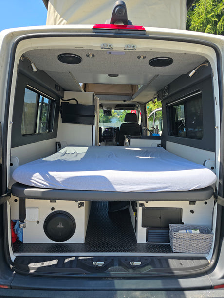 Spacious RV rental interior featuring a cozy bed, under-bed storage with subwoofer, and custom finishes for comfortable travel.