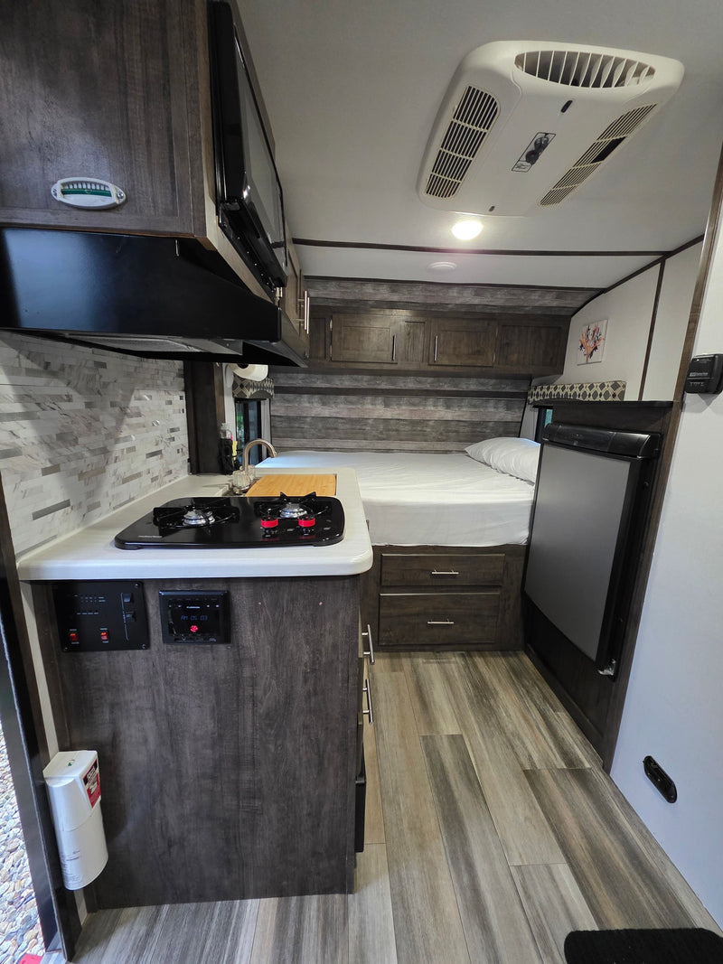 RV rental interior: kitchenette with stove, sink, and microwave, plus a comfortable bed area and refrigerator. Perfect for road trips. — photo 4