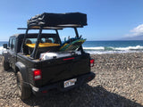 Black Jeep Gladiator with rooftop tent and surfboards on a rocky beach by the ocean. Ideal for an RV rental adventure.