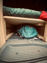 Cozy RV rental interior shows a green sleeping bag on a wooden bunk, with an Osprey backpack stored in the organized space below.