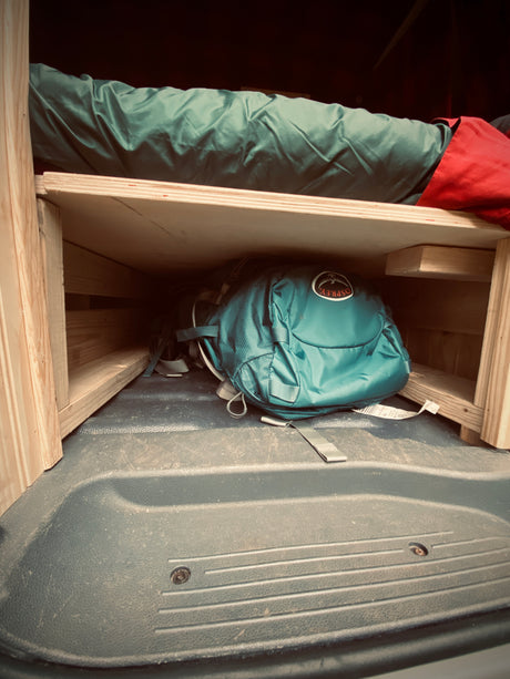 Cozy RV rental interior shows a green sleeping bag on a wooden bunk, with an Osprey backpack stored in the organized space below.