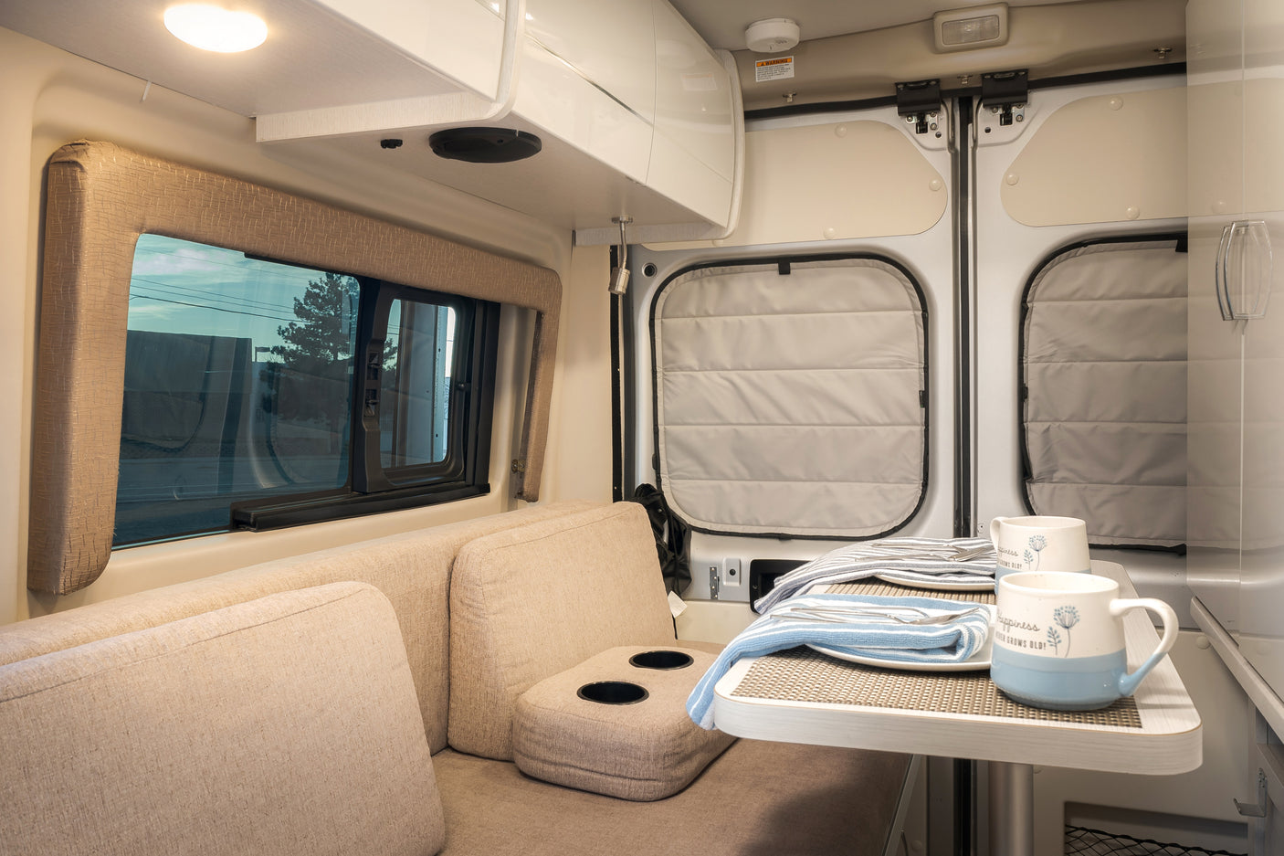 Interior of an **rv rental** showing comfortable seating, a dining table set for two, and a window view of the outdoors.