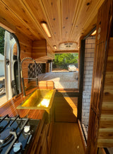 Explore this stylish RV rental's custom wood interior, featuring a kitchenette with a gold sink, comfy bed, and compact bathroom.