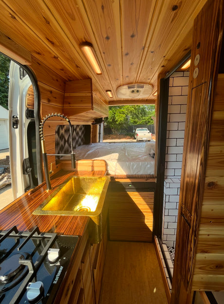 Explore this stylish RV rental's custom wood interior, featuring a kitchenette with a gold sink, comfy bed, and compact bathroom.