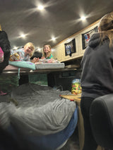 Two smiling girls are cozy on an RV rental bunk bed, ready for a family adventure. Inside a camper van at night.