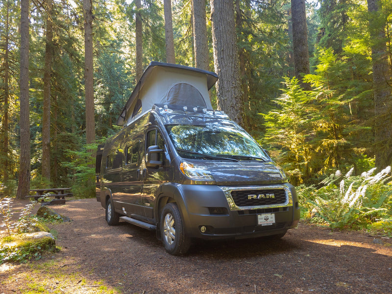  parked in a sun-dappled forest. Book your rv rental for nature escapes!|A dark grey pop-top RV rental van is parked in a beautiful — photo 9