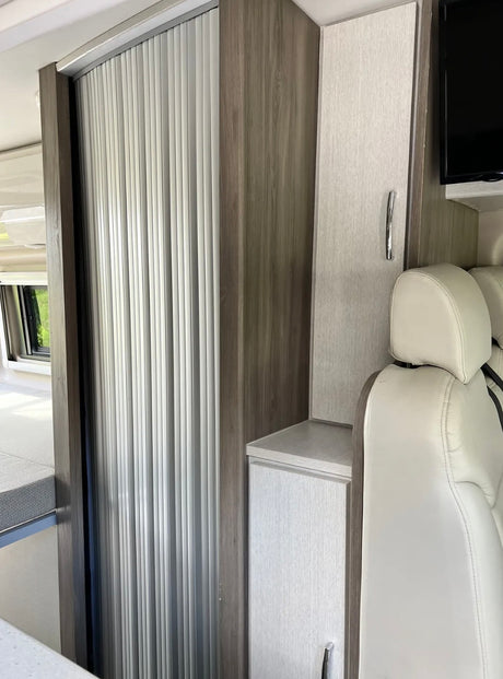 Compact RV rental interior featuring modern wood cabinetry, a roll-up door, and storage by the seat.