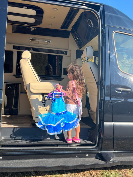 Child with blue dress enters a plush RV rental van. Its luxurious, custom interior is ready for adventure.