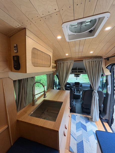 Stylish RV rental interior with wooden paneling, kitchen sink, overhead fan, and front cab privacy curtains.