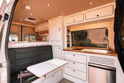  parked outdoors on a sunny day.|Modern white RV rental camper van interior. Side door open revealing a clean kitchen with cabinets — photo 2
