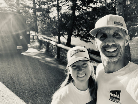 Smiling couple with their camper van rental on a scenic road, enjoying the outdoor adventure.