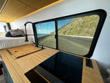 Stunning RV rental interior with kitchen, bed, and ocean road view from the window. Perfect for van life adventures!