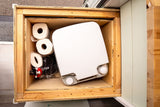 RV rental essential: a neatly stored portable toilet, toilet paper, and safety equipment in a wooden compartment.