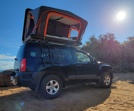 Explore the coast! Black SUV with a rooftop tent on sandy beach, offering a unique RV rental alternative for camping.