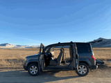 A versatile Honda Element with all doors open, parked in a scenic mountain field, ready for a road trip. Great RV rental alternative.