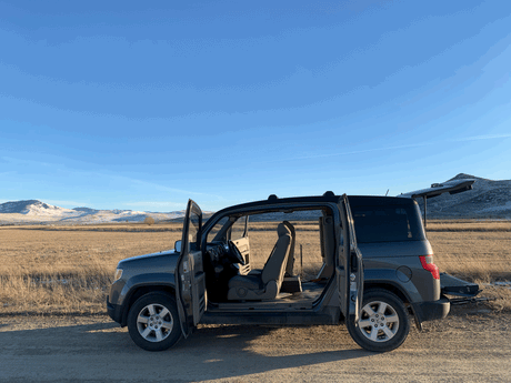 A versatile Honda Element with all doors open, parked in a scenic mountain field, ready for a road trip. Great RV rental alternative.