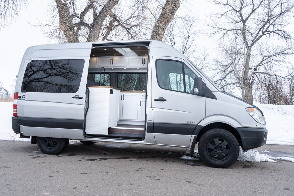 Sleek silver RV rental camper van. Open side door reveals a modern interior with white cabinets and wood accents.