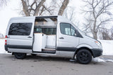 Sleek silver RV rental camper van. Open side door reveals a modern interior with white cabinets and wood accents.