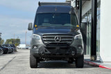Front view of a customized dark gray Mercedes-Benz Sprinter van with off-road tires and heavy-duty bumper. Ideal for RV rental adventures.