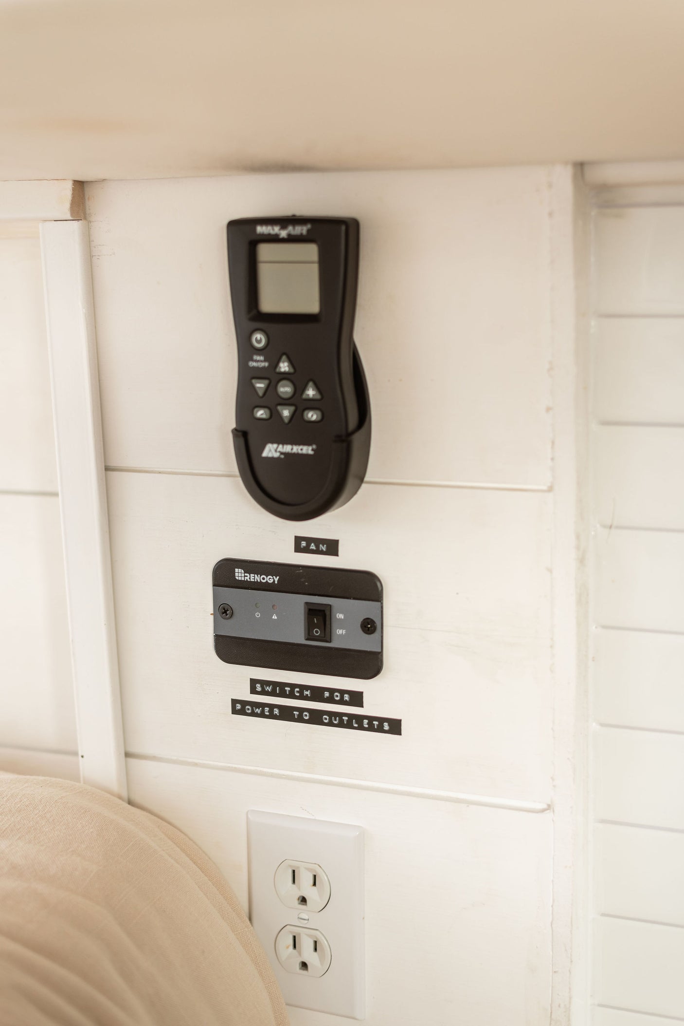 An RV rental's essential control panel featuring a Maxx Air fan remote, Renogy power switch, and AC outlets.