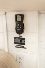 An RV rental's essential control panel featuring a Maxx Air fan remote, Renogy power switch, and AC outlets.