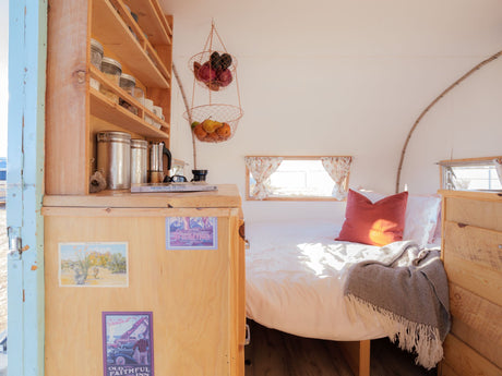 Experience comfort in this cozy rv rental: a bright bedroom with white bedding, wooden shelves, and hanging fruit baskets.