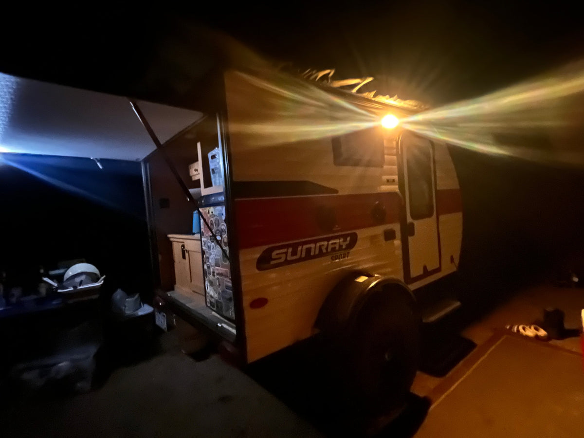 Illuminated Sunray Sport rv rental at night, with an open rear galley kitchen and extended awning. Ideal for travel and camping. — photo 17