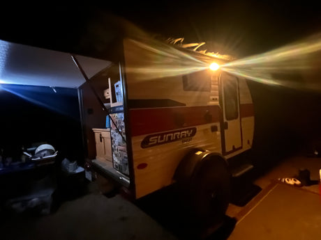 Illuminated Sunray Sport rv rental at night, with an open rear galley kitchen and extended awning. Ideal for travel and camping.