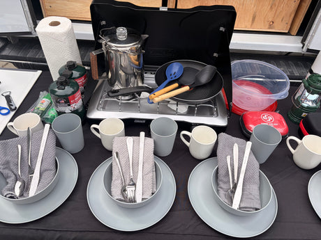 Perfect RV rental kitchen setup: Coleman stove, coffee percolator, propane, utensils, and dinnerware for convenient camping meals.