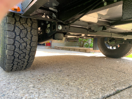 Low-angle view of an RV rental's undercarriage: rugged tire, robust suspension, and protective wiring, ready for the road.