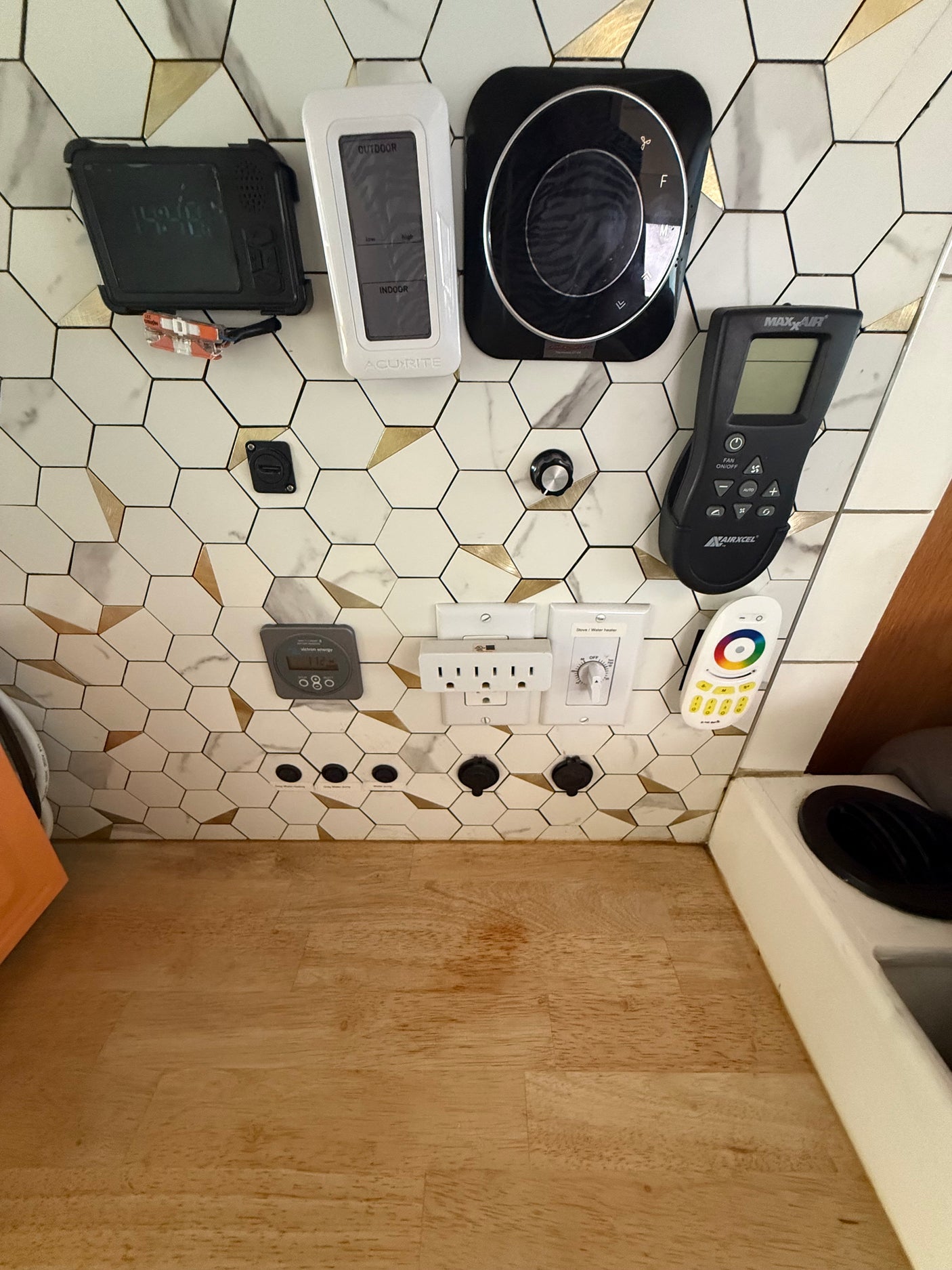 RV rental command center: AcuRite temp, MaxxAir fan, Victron power, stove controls, and outlets on a hexagon tile backsplash.