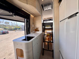 Bright RV rental interior showing a modern kitchen, built-in fridge, and bunk bed access.