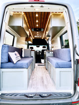Spacious RV rental interior with custom wood ceiling, cozy blue cushions, and a functional layout, perfect for mobile adventures.