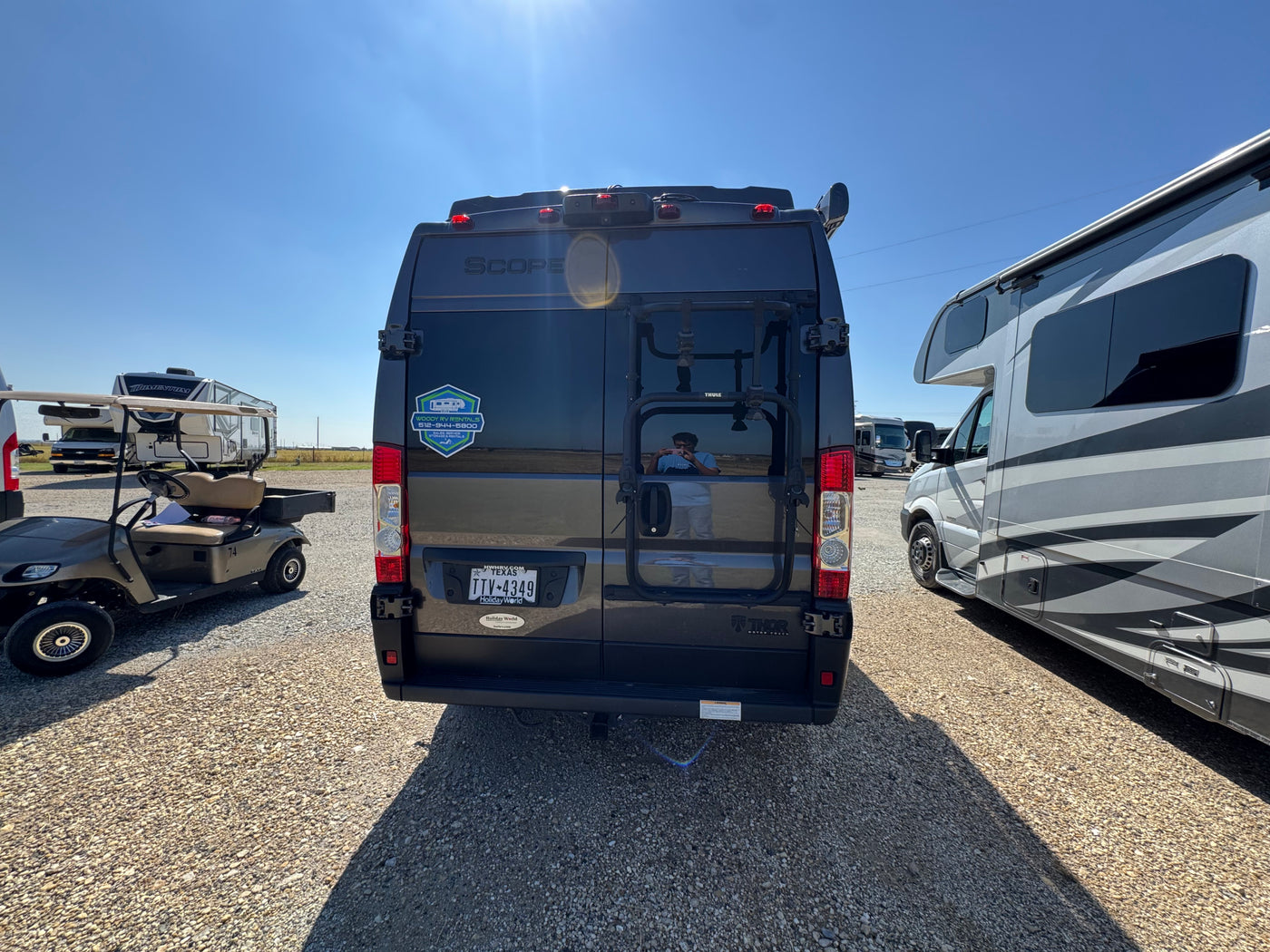 A black Thor Scope RV rental camper van is parked in a sunny gravel lot, surrounded by other RVs and a golf cart. — photo 3