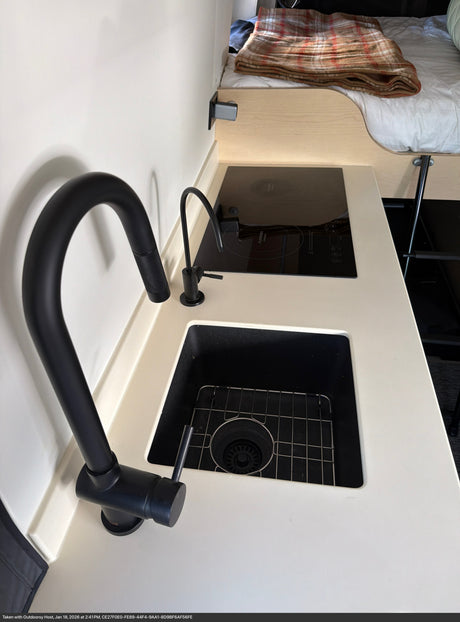 Modern RV rental kitchen with black sink, gooseneck faucet, water filter, and Furrion induction cooktop.