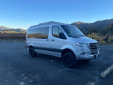 Silver Mercedes-Benz Sprinter camper van, perfect for RV rental adventures, parked in a sunny vineyard with hills.