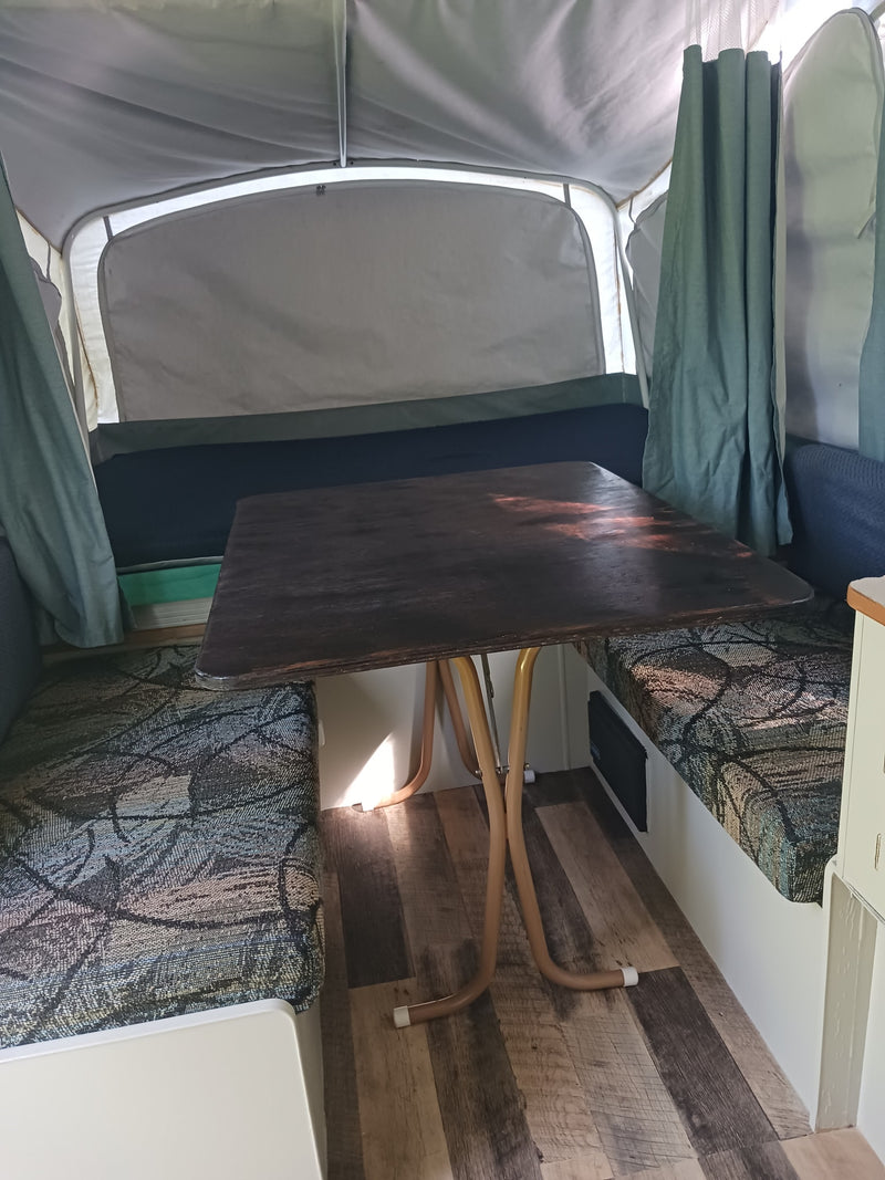RV rental: Inside a pop-up camper featuring a dark wooden table, patterned benches, and light fabric walls. — photo 6