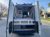 Open rear doors reveal the spacious interior of this RV rental, featuring a bed, storage, and modern design.