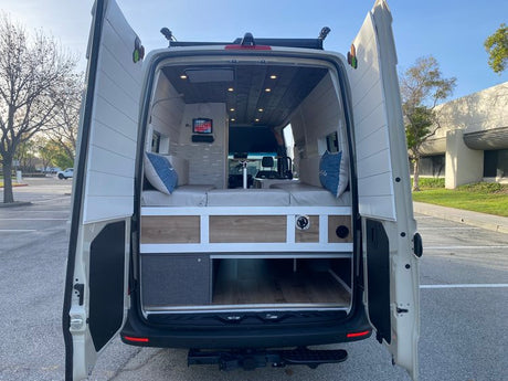 Open rear doors reveal the spacious interior of this RV rental, featuring a bed, storage, and modern design.