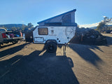 RV rental: Mission Overland pop-up trailer, hitched to a truck, set up for outdoor camping with long shadows.