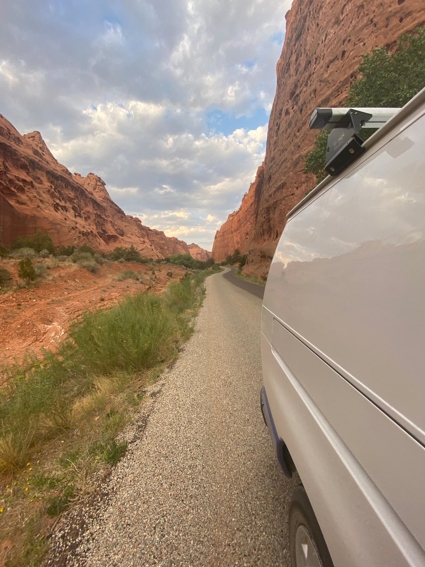 White rv rental van parked on a gravel road in a striking red rock canyon, winding through desert landscape under a cloudy sky.