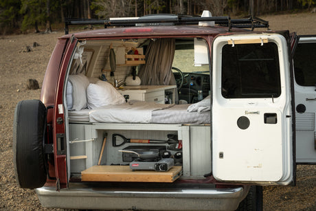 Inside this custom camper van, ideal for RV rental, a bed, kitchen, and pull-out stove are visible.