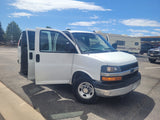A white van with open doors is parked; a large RV rental and other vehicles are visible in the sunny background.