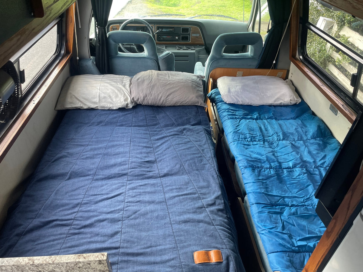 Cozy rv rental interior: two blue beds, pillows, and a view into the driver's cabin and windows. Perfect for travel! — photo 9