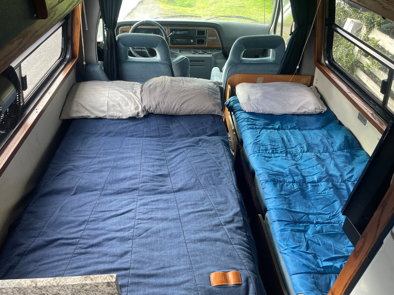 Cozy rv rental interior: two blue beds, pillows, and a view into the driver's cabin and windows. Perfect for travel! — photo 9