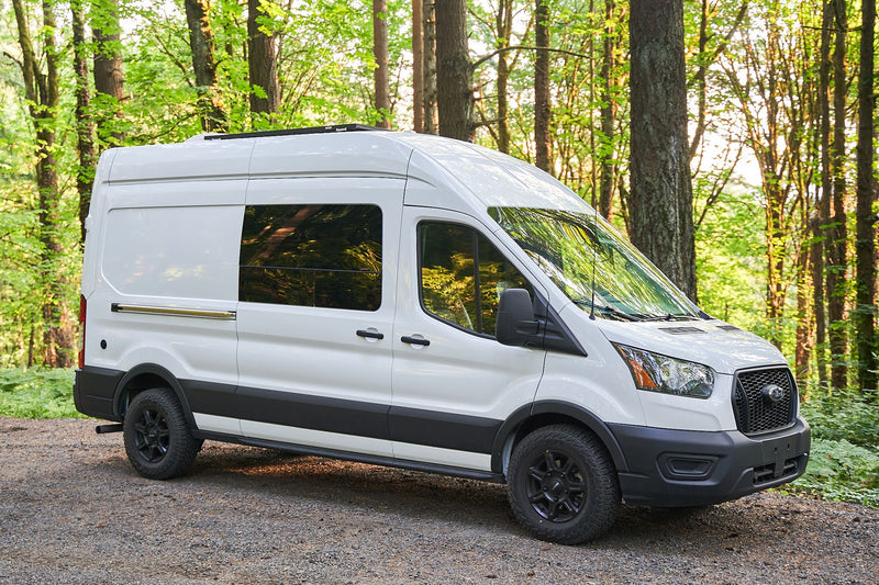  showing its kitchen and living space. Parked on a gravel path in a sunny forest.|Modern white camper van for RV rental — photo 2